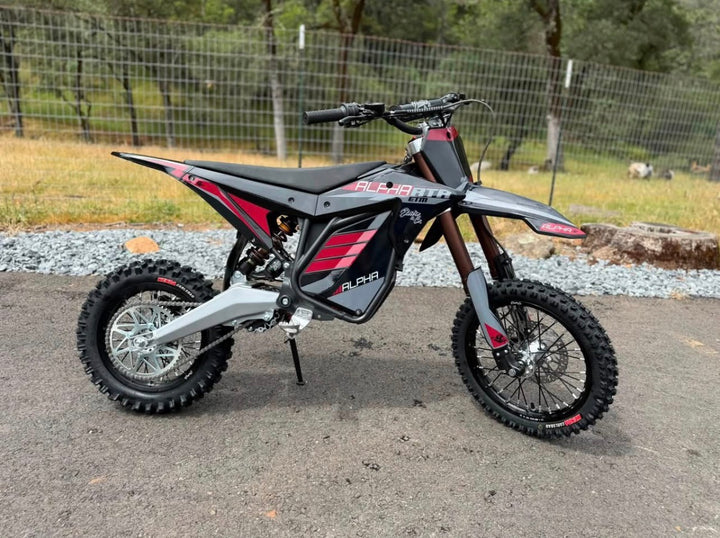 Black and red dirt bike on a paved surface with a fence and trees in the background