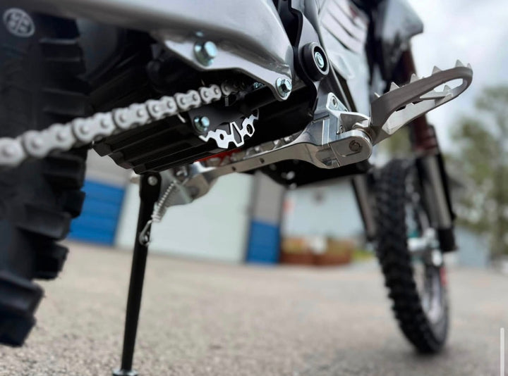 Close-up of a motorcycle chain and foot pegs with blurred background
