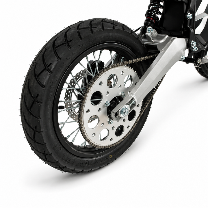 Close-up of a motorcycle's rear wheel, featuring a black knobby tire, silver multi-spoke wheel, disc brake, chain drive, and silver swing arm on a white background.