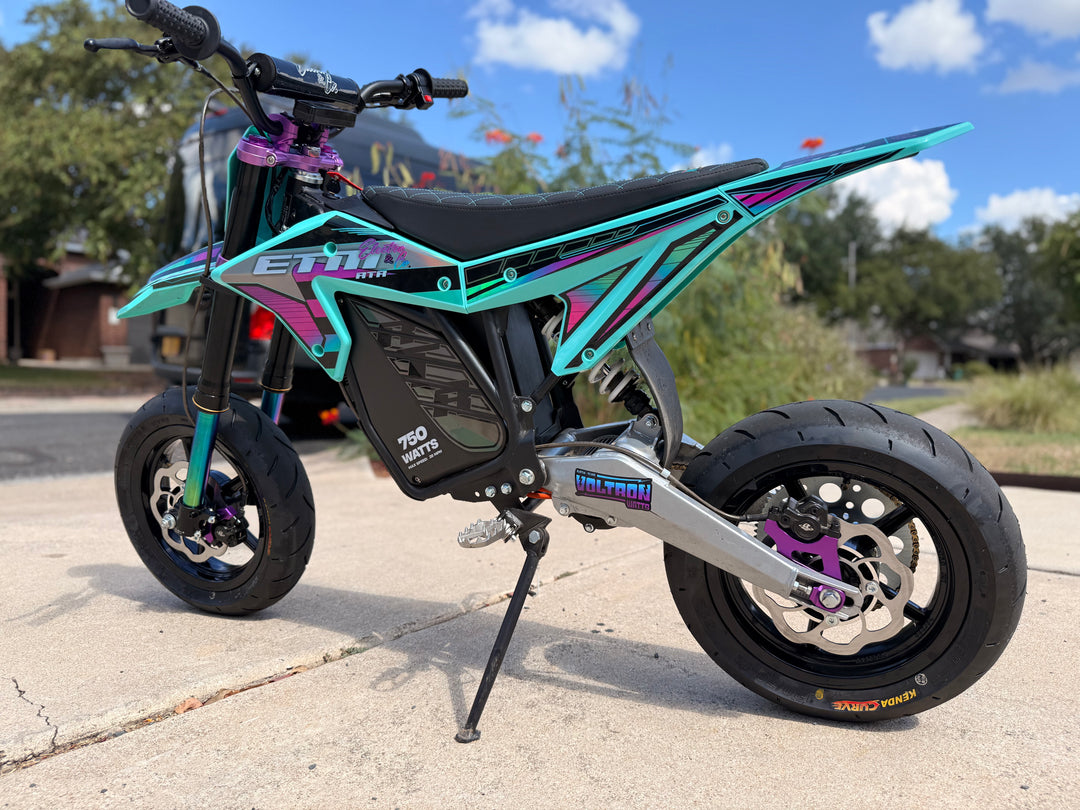 Turquoise and black electric bike on a driveway with trees and a house in the background