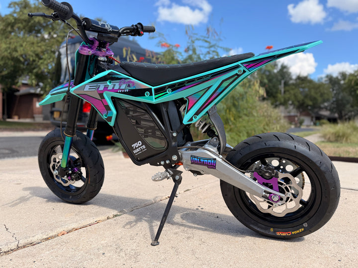 Turquoise and black electric bike on a driveway with trees and a house in the background