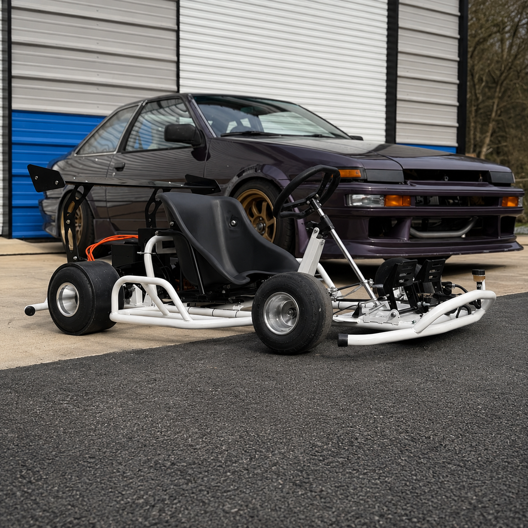 A custom-built go-kart with a white tubular frame, black seat, and black tires, positioned in front of a dark purple Nissan Skyline R32 car on asphalt in front of a garage door.