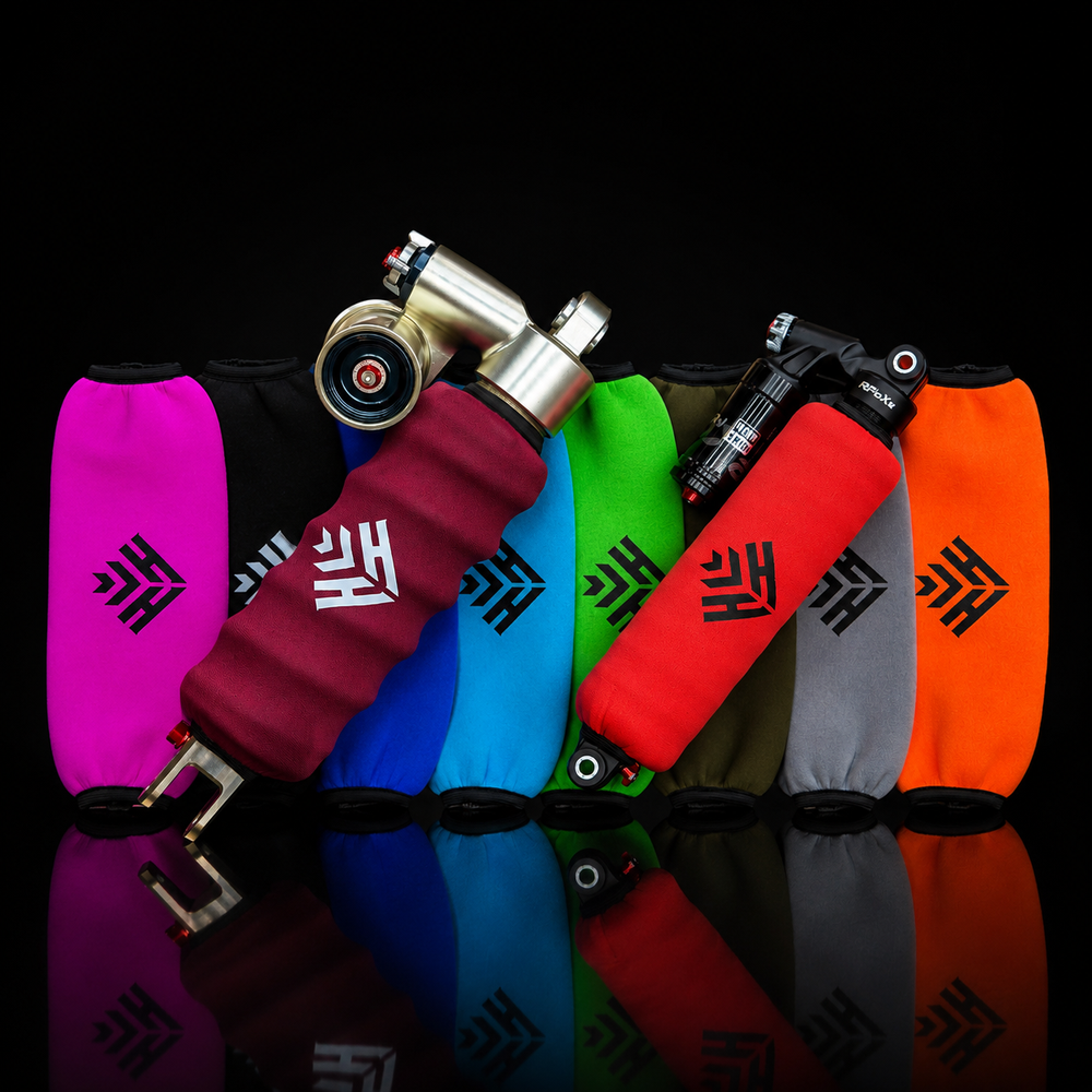 Six bicycle handlebar grips in different colors (magenta, black, burgundy, blue, green, red, gray, and orange) lined up on a reflective black surface. Each grip features a black geometric logo and the white text 'FA'.