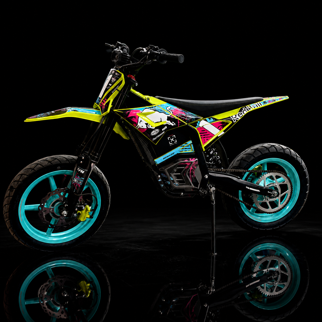 A small off-road dirt bike with a vibrant multicolor graphic wrap, featuring neon yellow, pink, blue, and black, standing on its kickstand against a black background with a reflective floor.